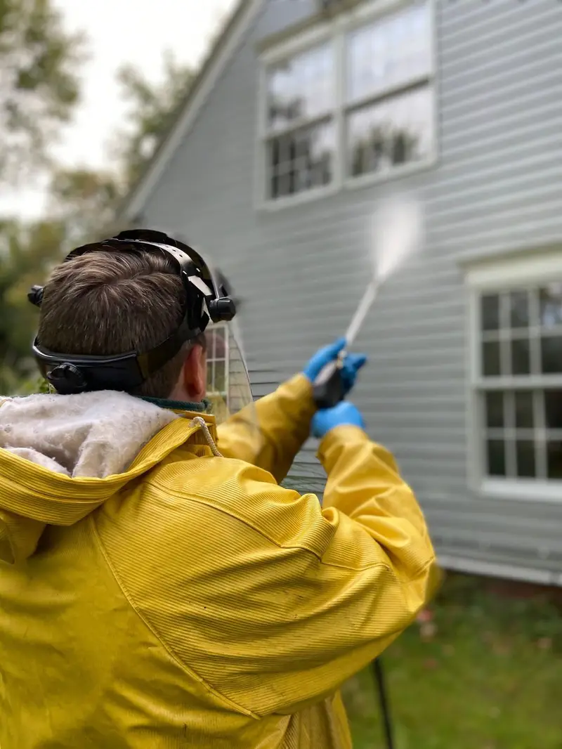 Pressure washing operative in protective clothing cleaning a house exterior
